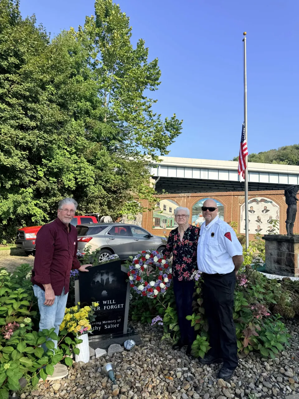 Family members and a firefighter in dress uniform stand together at Cathy's memorial stone beside the new wreath.